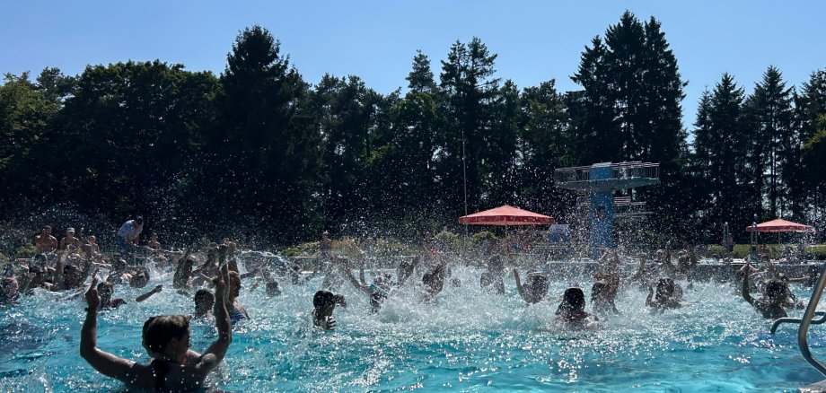 Freibad Miesau Ein turkisblaues Schwimmbad mit Badegästen in im Hintergrund grüne Bäume und blauer Himmel.