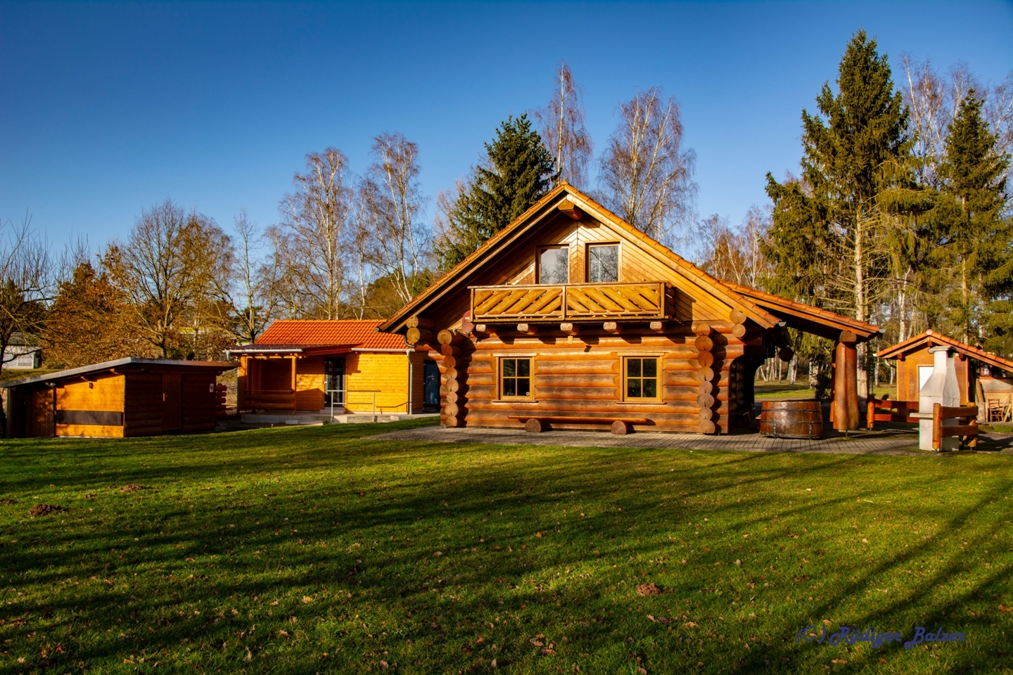 Blockhütte mit Nebengebaüden aus Holz auf einer grünen Wiese. 