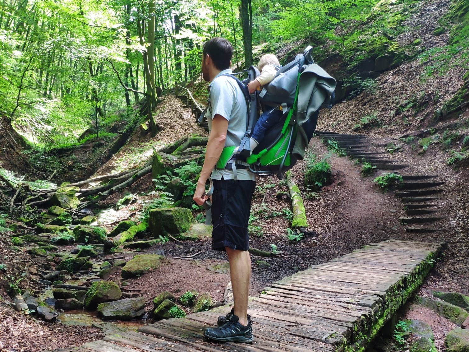 Elendsklamm Mann mit Kind auf dem Rücken, die im Wald auf einer Holzbrücke stehen, die über einen Bach reicht.