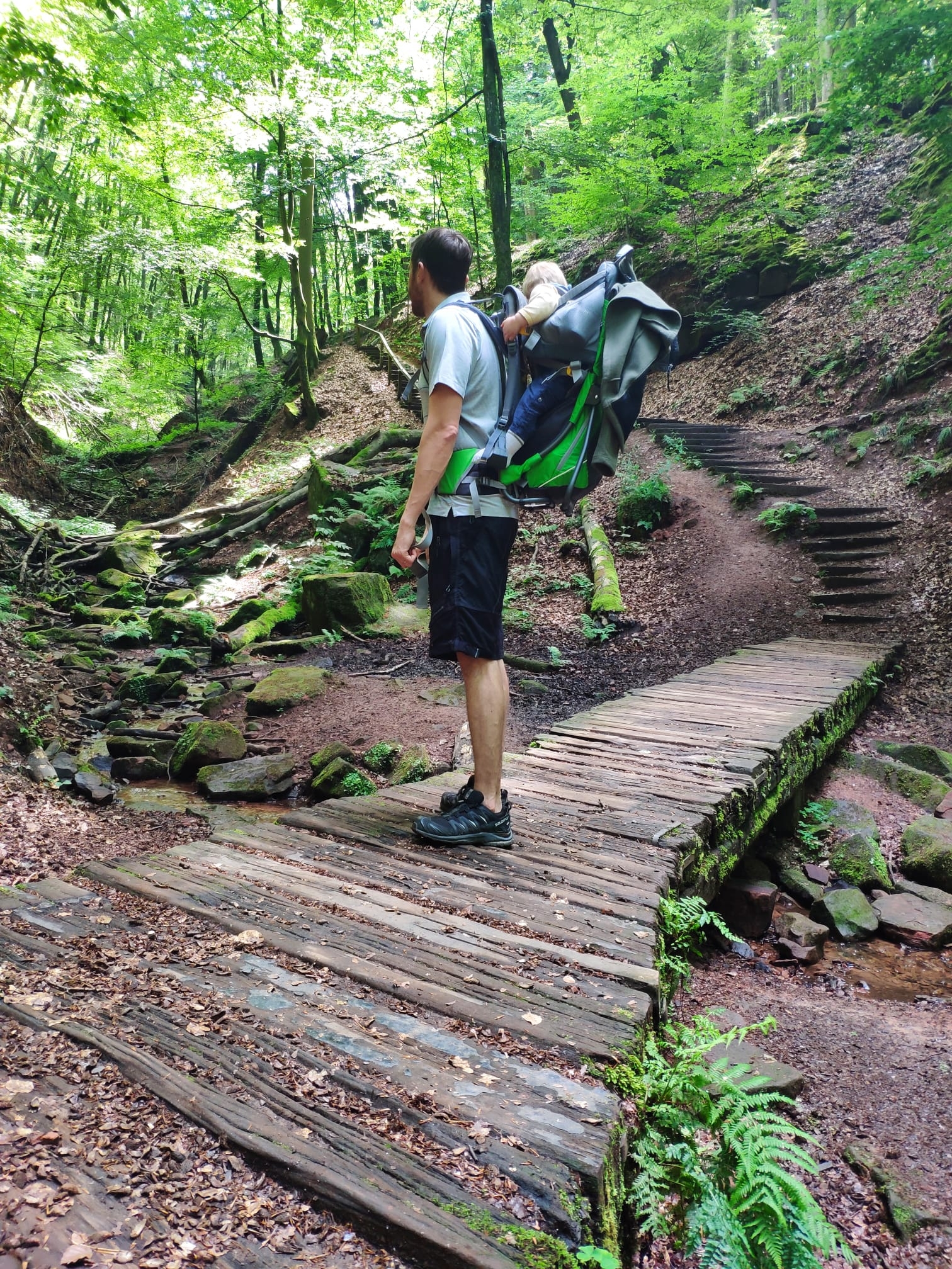 Elendsklamm Mann mit Kind auf dem Rücken, die im Wald auf einer Holzbrücke stehen, die über einen Bach reicht.