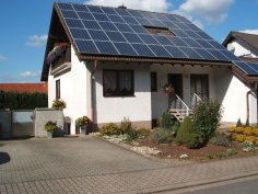 Einfamilienhaus mit Vorgarten und Solarpanel auf dem Dach.