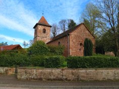 Kleine rote Sandsteinkirche, die durch eine Hecke eingesäumt wird.