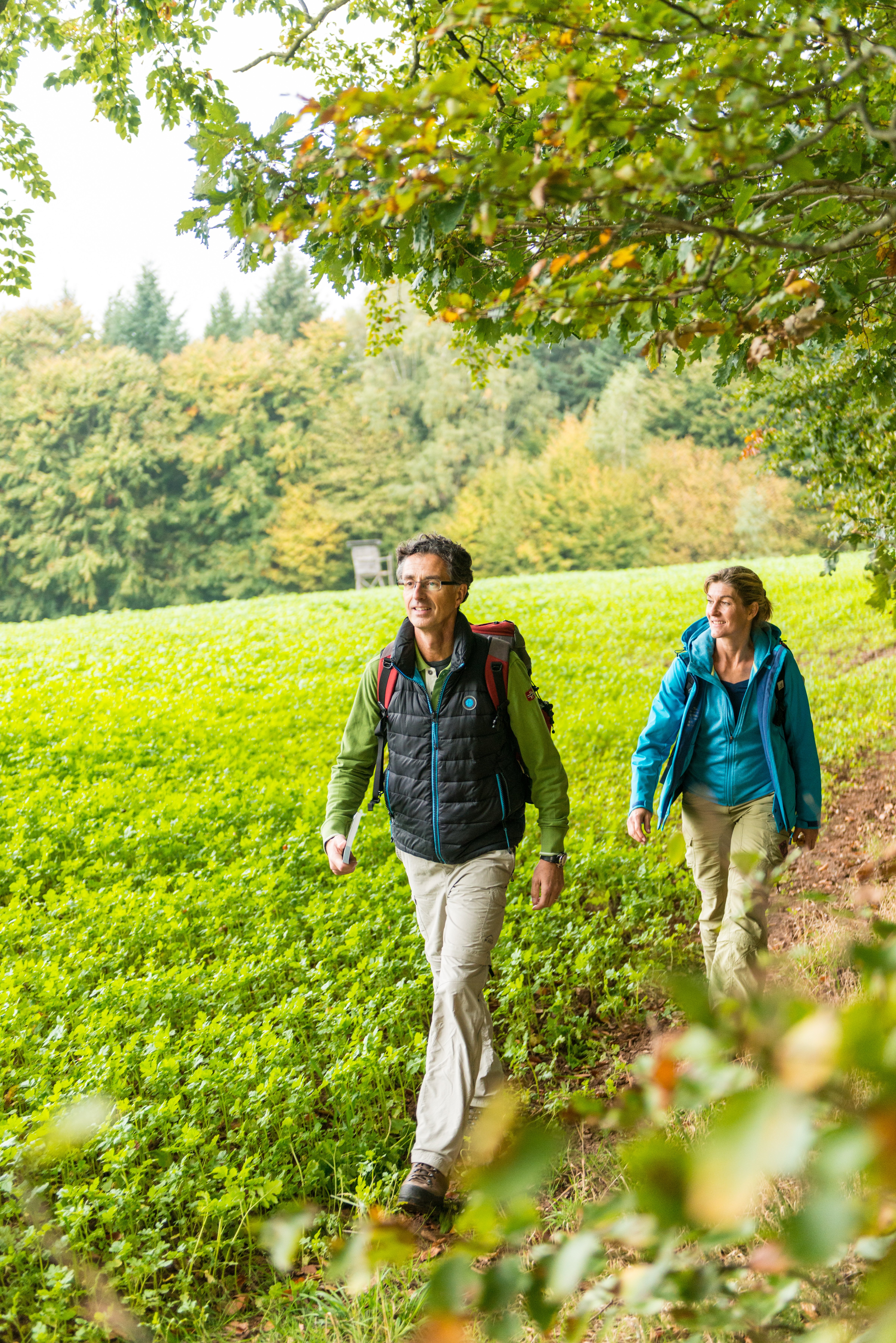 Eine Frau und ein Mann laufen auf einem unbefestigten Weg entlang einer Wiese