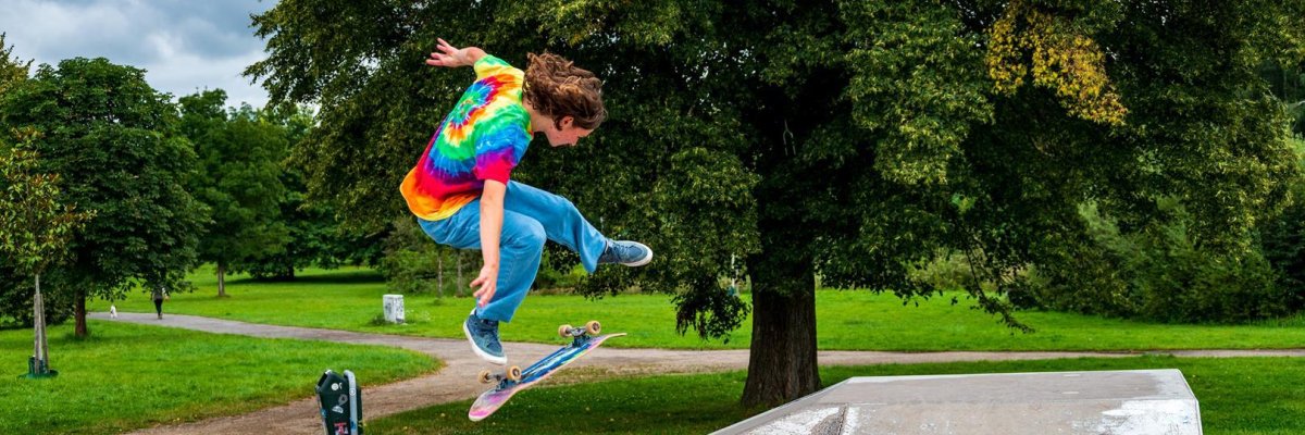 Skater_Ferienprogramm Junge im bunten T-Shirt der mit Skatboard springt