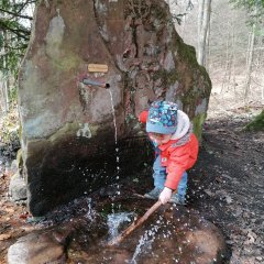 Kind das am Becken, in dem das Wasser vom Steinbrunnen fließt, mit einem Stock spielt